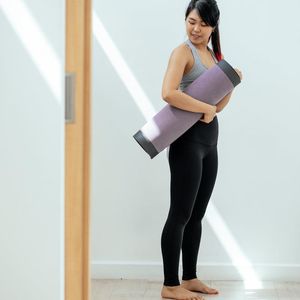 A rolled-up grey yoga mat standing against a light wall.